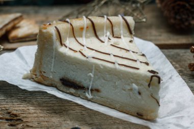 Ahşap arka plan üzerinde beyaz kağıt üzerinde güzel ev yapımı pasta peynirli kek. Sonraki çikolatalı kurabiye, Noel hediyeleri, yılbaşı ağacı, koni ve oyuncaklar. Yılbaşı kutlamak için gebe.