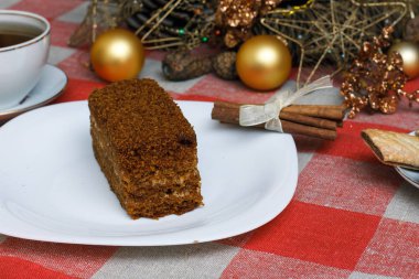 Damalı bir masa örtüsü ile çay, bisküvi, tarçın bir yılbaşı Noel ağacı bir arka plan üzerinde beyaz bir tabağa kek. Yeni konsept. Tatil için.