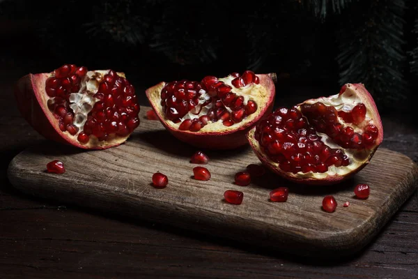 Cut part of pomegranate on a wooden board on a wooden background on the background of trees. New Year's holiday. tree branch — Stock Photo, Image