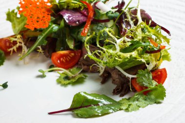 Büyük beyaz ahşap bir masa üzerinde bir beyaz masa örtüsü tabağa restoranda için sebze salata menüsü. Bıçak ve çatal ile masada salata. Svezhive sebze.