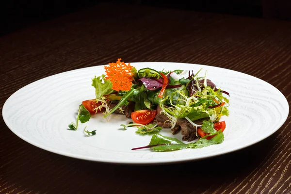 Büyük beyaz ahşap bir masa üzerinde bir beyaz masa örtüsü tabağa restoranda için sebze salata menüsü. Bıçak ve çatal ile masada salata. Svezhive sebze.