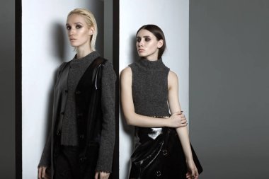 Moda fotoğrafçılığı. Davetli tasarımcı Atölyesi gri bir arka plan üzerinde siyah ve gri elbiseli kız. Kız sarışın raslablennoy poz. Kız esmer poz. Reklam elbise