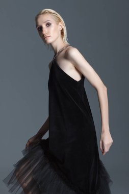 Moda fotoğrafçılığı. Studio gri bir arka plan üzerinde elbise kız siyah Tasarımcısı. Kız sarışın raslablennoy poz. Reklam elbise.