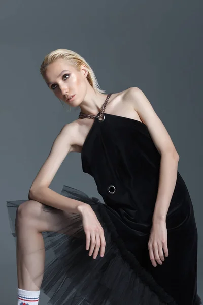 Fashion photography. Girl in black designer dress in the studio on a gray background. Girl blonde in raslablennoy pose. Advertising clothes.