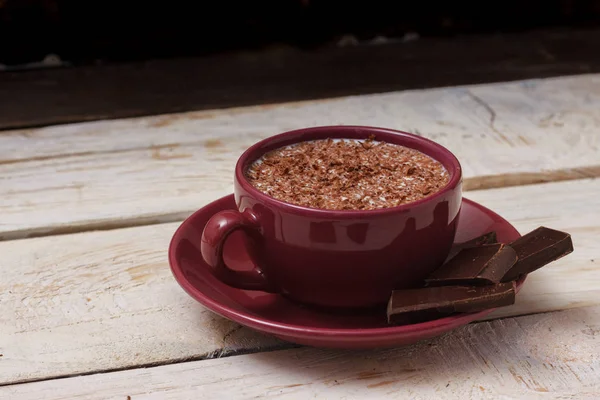 Chocolate de leite em uma xícara em um pires em um fundo de madeira leve — Fotografia de Stock