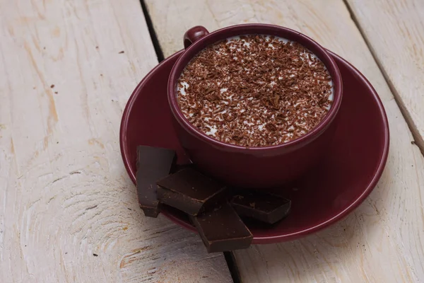 Milk chocolate in a cup on a saucer on a wooden background. Clos
