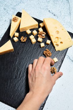 Pieces of cheese on a dark background. Cheeseboard. Sliced apple and nuts on the board. 