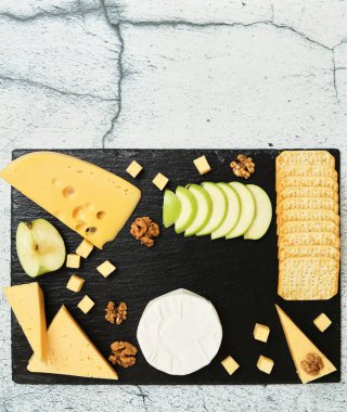 Pieces of cheese on a dark background. Cheeseboard. Sliced apple and nuts on the board. 