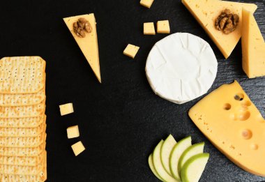 Pieces of cheese on a dark background. Cheeseboard. Sliced apple and nuts on the board. 