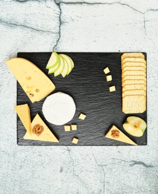 Pieces of cheese on a dark background. Cheeseboard. Sliced apple and nuts on the board. 