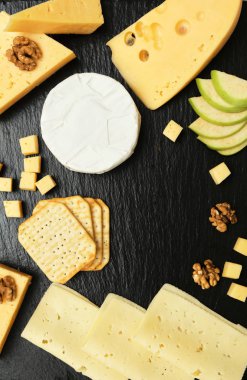 Pieces of cheese on a dark background. Cheeseboard. Sliced apple and nuts on the board. 