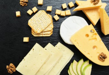 Pieces of cheese on a dark background. Cheeseboard. Sliced apple and nuts on the board. 