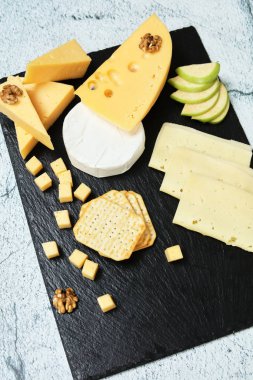 Pieces of cheese on a dark background. Cheeseboard. Sliced apple and nuts on the board. 