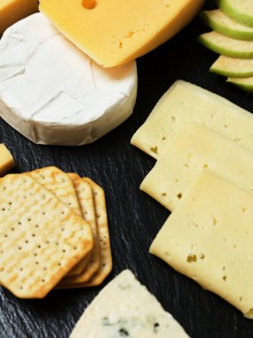 Pieces of cheese on a dark background. Cheeseboard. Sliced apple and nuts on the board. 