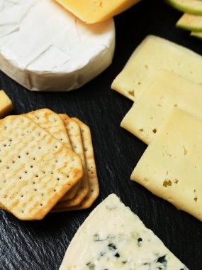 Pieces of cheese on a dark background. Cheeseboard. Sliced apple and nuts on the board. 