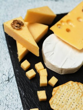 Pieces of cheese on a dark background. Cheeseboard. Sliced apple and nuts on the board. 