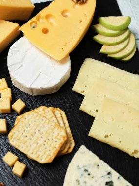 Pieces of cheese on a dark background. Cheeseboard. Sliced apple and nuts on the board. 