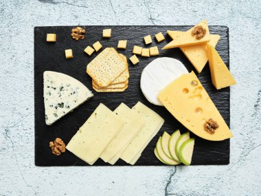 Pieces of cheese on a dark background. Cheeseboard. Sliced apple and nuts on the board. 