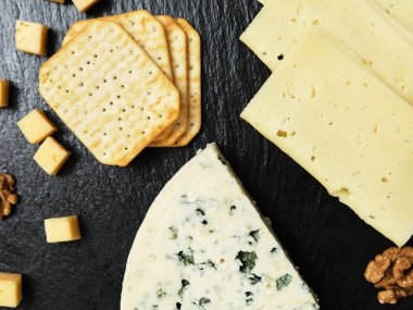 Pieces of cheese on a dark background. Cheeseboard. Sliced apple and nuts on the board. 