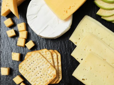 Pieces of cheese on a dark background. Cheeseboard. Sliced apple and nuts on the board. 