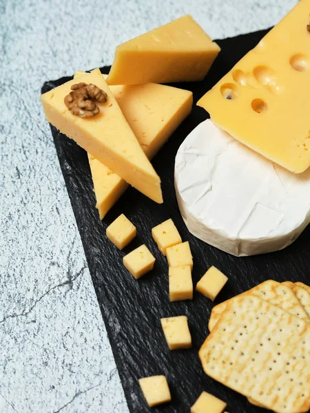 Pieces of cheese on a dark background. Cheeseboard. Sliced apple and nuts on the board. 