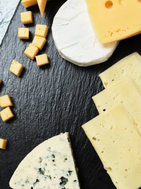 Pieces of cheese on a dark background. Cheeseboard. Sliced apple and nuts on the board. 