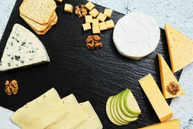 Pieces of cheese on a dark background. Cheeseboard. Sliced apple and nuts on the board. 