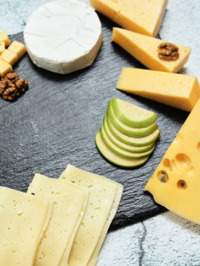 Pieces of cheese on a dark background. Cheeseboard. Sliced apple and nuts on the board. 