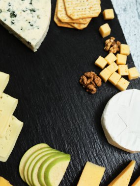 Pieces of cheese on a dark background. Cheeseboard. Sliced apple and nuts on the board. 