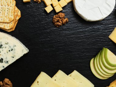 Pieces of cheese on a dark background. Cheeseboard. Sliced apple and nuts on the board. 