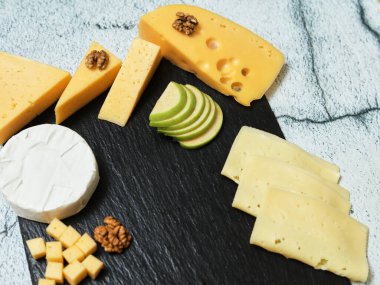 Pieces of cheese on a dark background. Cheeseboard. Sliced apple and nuts on the board. 