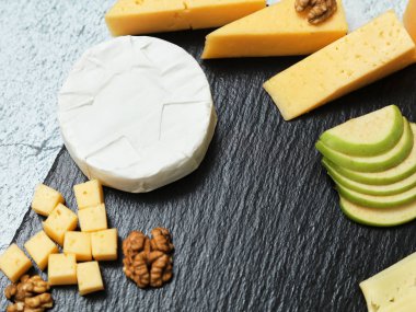Pieces of cheese on a dark background. Cheeseboard. Sliced apple and nuts on the board. 