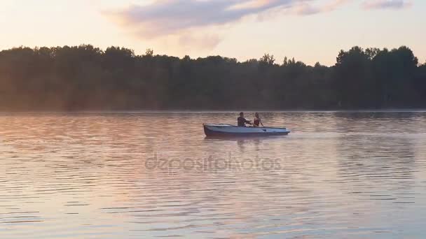 Una pareja amorosa cabalgando en un bote de remos en el río en tiempo de puesta de sol dorada. La luz dorada del sol en la superficie del agua del lago. Atardecer dorado amanecer en el lago . — Vídeo de stock