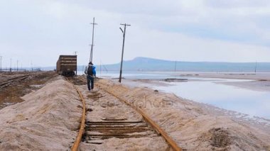 Erkek demiryolu ile gider. Üzerinde bağları için eski arabalar yürüyen turist. Eski paslı demiryolu ile Tuz Gölü. Tuzlu Tuz Gölü Baskunchak Rusya