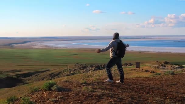 Un hombre se para en la montaña y extiende sus manos. El hombre con mochila subió a una montaña y mirando hacia abajo puso las manos arriba — Vídeo de stock