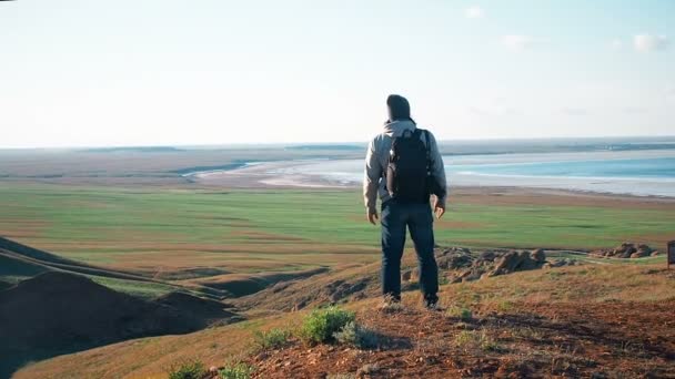 Ένας άνδρας στέκεται στο βουνό και απλώνεται τα χέρια της. Ο άνθρωπος με το σακίδιο ανέβηκε ενός βουνού και κοιτάζοντας προς τα κάτω Βάλτε τα χέρια σας — Αρχείο Βίντεο