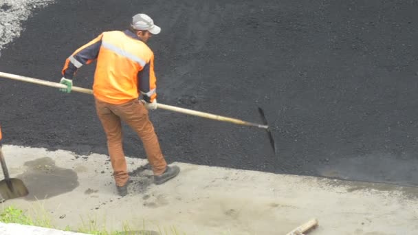 Domodědovo, Rusko - 17. května 2017: Silniční stavební dělník vyrovnání pomocí hrábě asfalt. Pracovník distribuuje horký asfalt na úseku silnice — Stock video