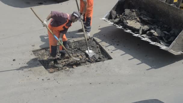 Domodedovo, russland - 17. Mai 2017: Straßenarbeiter laden Stücke alten Asphalts in einen Planierraupeneimer. Reparaturabschnitt der Fahrbahndecke. Arbeiter entfernten Asphaltschicht. — Stockvideo