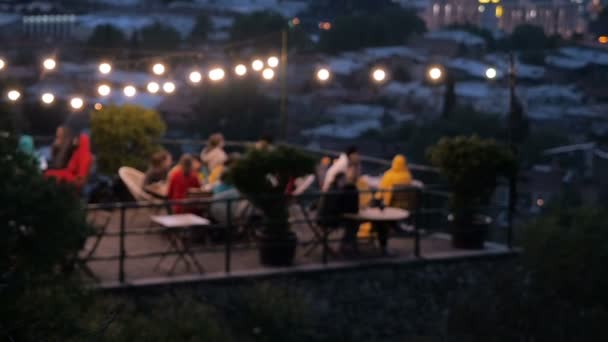 Oskärpa videofilmer. Människor vilar i ett mysigt café på terrassen på kvällen. Restaurangen på terrassen. Chillout bar på backen med panoramautsikt över stadens kväll. — Stockvideo