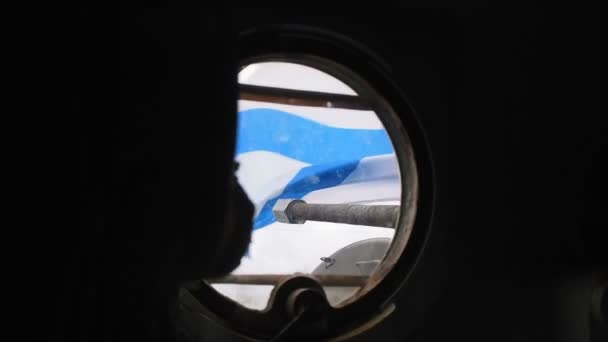 Desde la ventana redonda de un portatropas blindado se ve una bandera azul-blanca en desarrollo y cañón de cañón — Vídeo de stock