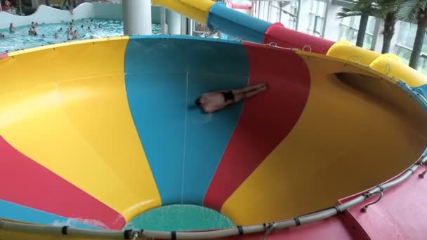 Ein junger Mann rutscht von einer Wasserrutsche in einem Wasserpark Leute reiten von der Rutsche und springen ins Becken — Stockvideo