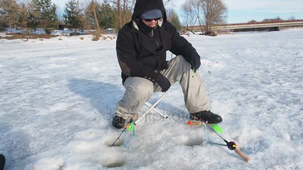 A fisherman fishing on winter fishing fish from a hole in the ice. A man is sitting on a pond holding a fishing rod in his hands. Winter activity — Stock Footage Fisherman Fishing Winter Fishing Fish Hole Ice Man Sitting Pond Stock Footage