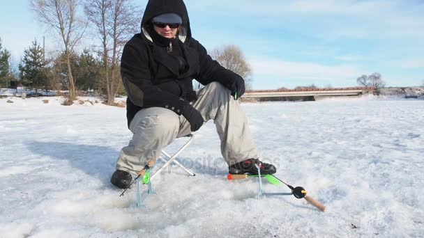 冬の氷の穴から魚を釣りに釣り漁師 彼の手で釣り竿を保持池に座っています 冬の活動 — ストック動画