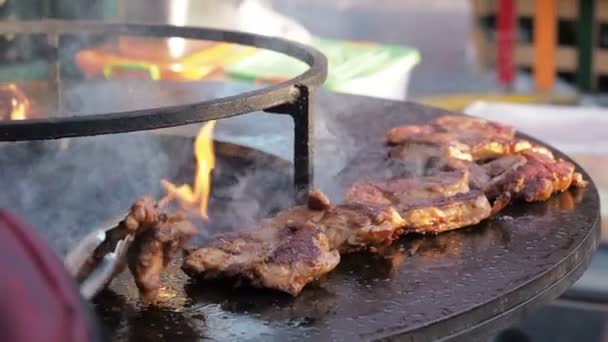 De man-kok verandert vlees op de grill. Mannen koken gegrild vlees. Close-up van de handen van de chef-koks die flip-over rauwe kippenvlees op de ronde barbecue. Straatvoedsel — Stockvideo