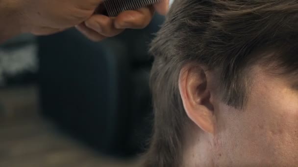 Friseur schneidet dem Kunden in einem Salon Haare an Schläfe und Ohr. Mann sitzt im Friseursessel, während er im Friseurladen mit der Schere schert. — Stockvideo