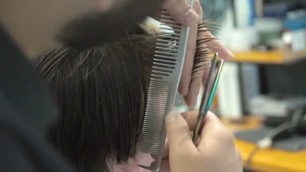 Friseur schneidet dem Kunden in einem Salon Haare an Schläfe und Nacken. Mann sitzt im Friseursessel, während er im Friseurladen mit der Schere schert. — Stockvideo