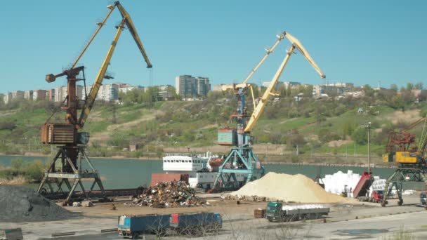 Landschaft der Schlepper und Kräne in der Werft im Frachthafen. Verladung von Baumaterial in LKWs in einem Frachtterminal. Ein großer Eimer sammelt Sand auf. — Stockvideo
