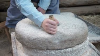 Tahıllı antik quern taş el değirmeni. Adam bir değirmen taşının yardımıyla tahılı un haline getiriyor. Erkek eli değirmen taşını döndürür. İnsan eliyle döndürülmüş eski öğütücü taşlar.