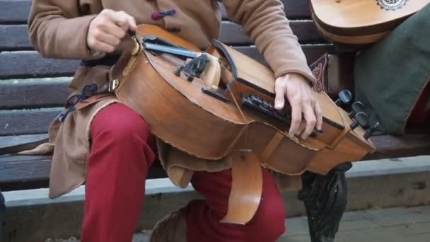 Уличный музыкант, одетый в винтажную этническую восточную одежду, играет музыку на традиционном ближневосточном музыкальном инструменте "хёрди-гёрди", также называемом "колесной скрипкой" — стоковое видео