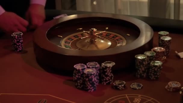 Крупье складывает фишки на стол рулетки, готовясь принимать ставки от игроков казино. Размещение стола в рулетке при низком освещении — стоковое видео